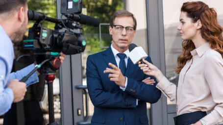professional cameraman and news reporter talking with serious businessman